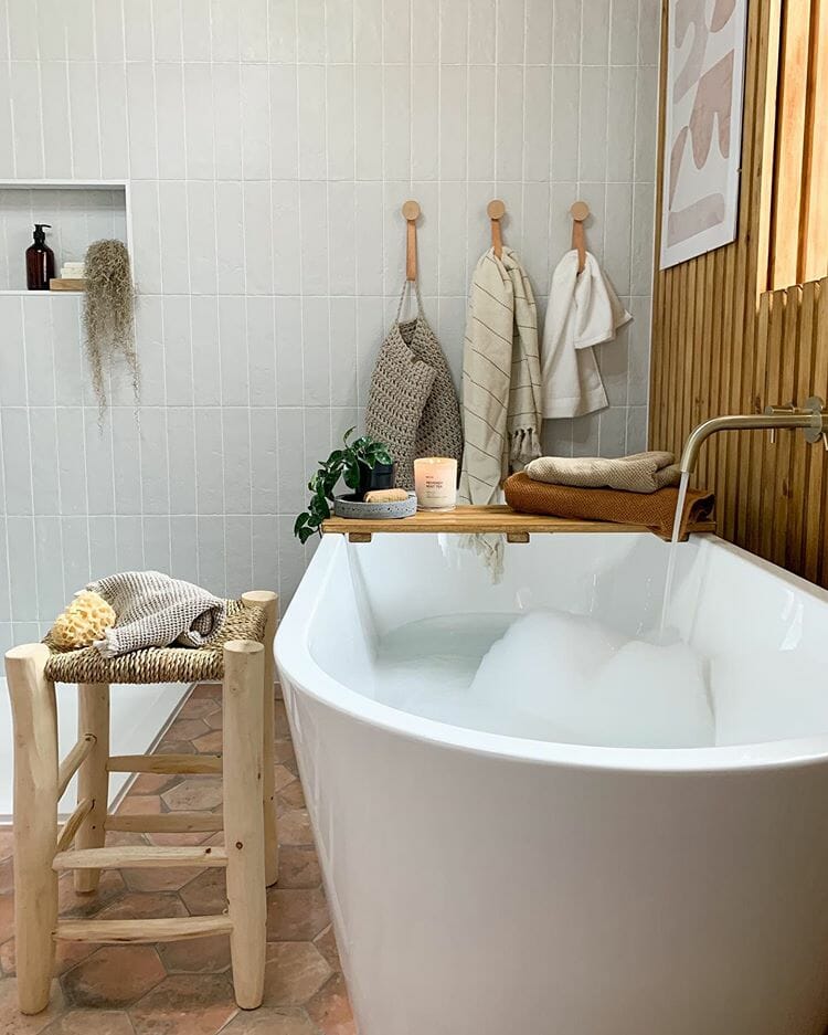 A large white bathtun filled with bubbles in a wooden scandi style bathroom