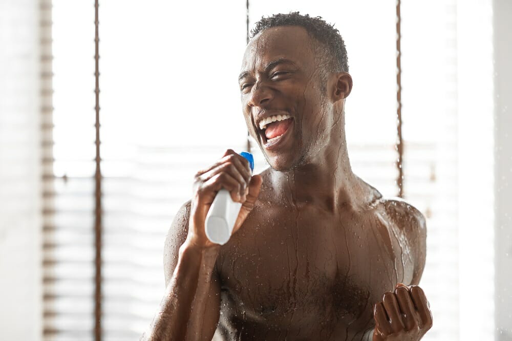 a half naked man using a bottle of shampoo as microphone while singing in the shower
