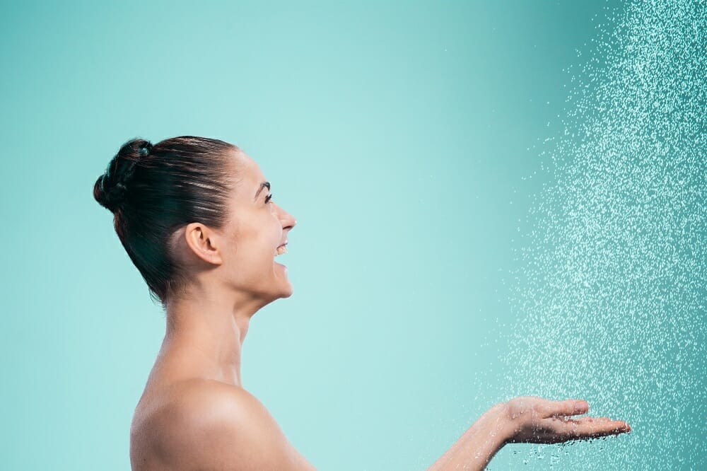a smiling woman putting her hands under a shower spray