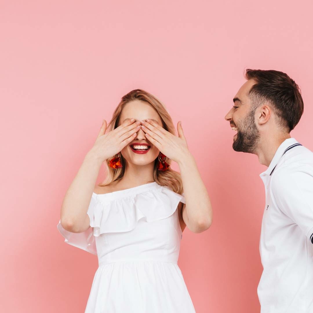 a woman covering her eyes as a man waits to give her a present