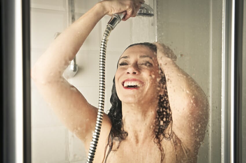 Happy woman using hand shower in a shower enclosure