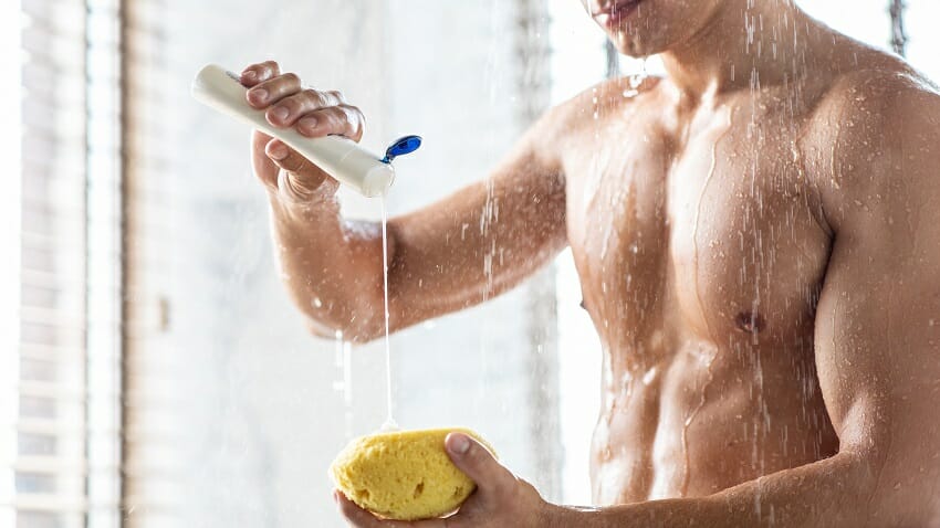 Man in the shower squeezing shampoo onto a sponge