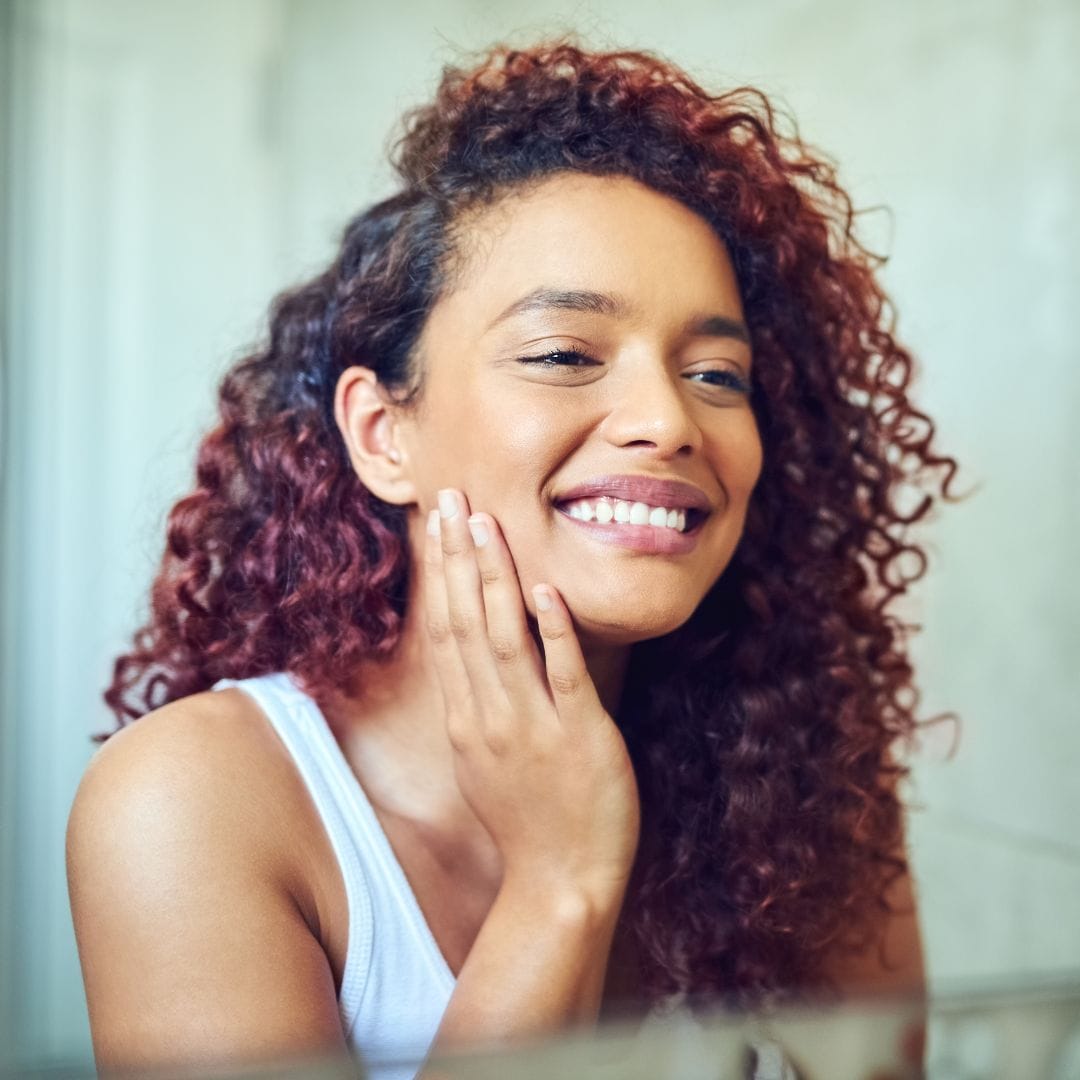 Woman with good skin smiling while looking into a mirror