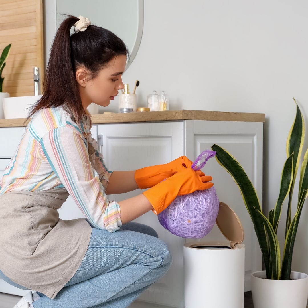 Woman with orange gloves cleaning bathroom bin