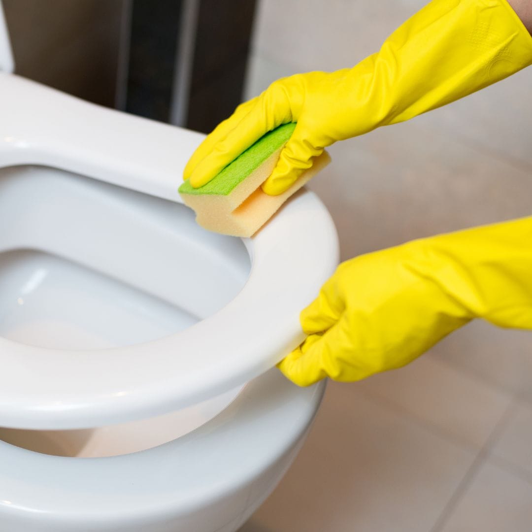 Cleaning the toilet bowl while wearing yellow rubber gloves