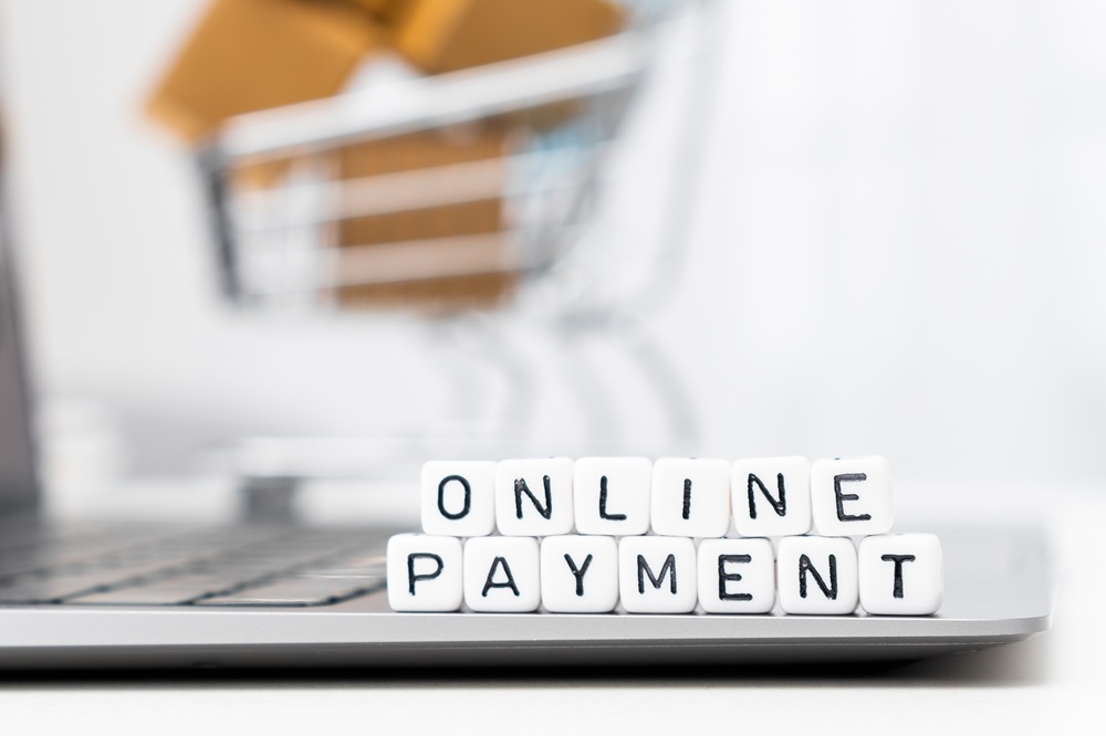 Online payment words on cubes laying on the laptop and a toy shopping cart with carton boxes serves as the background.